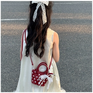 Enfant portant un mini sac rouge à pois avec nœud en perles lors d'une vue en extérieur
