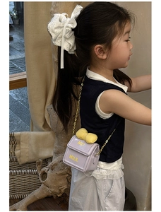 Détail d'un enfant portant un sac bandoulière violet clair avec nœud jaune et chaîne