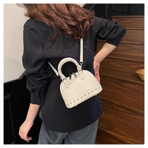 Detailed view of white crocodile pattern shell bag with silver rivets on wooden stairs