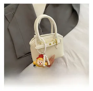 Close-up of beige shell handbag with grain texture, gold hardware, and doll charm