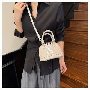 Detail showing the crocodile texture and silver studs on the cream shell bag worn crossbody