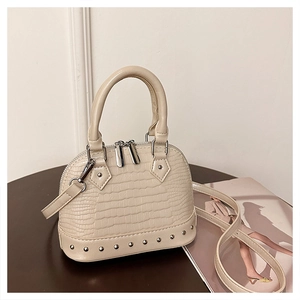 Detail of beige crocodile pattern shell bag featuring silver studs and metallic zippers