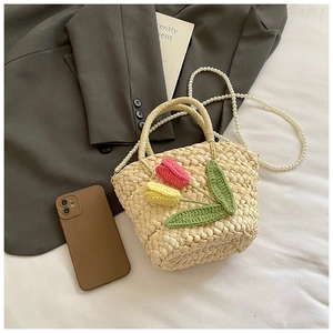 Detail of straw woven bag with handmade crochet flowers and elegant pearl strap
