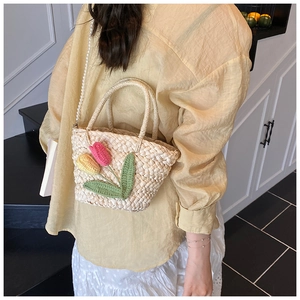 Detail of handmade straw bag with crochet tulips and pearl strap on model