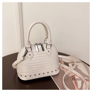 Close-up of cream shell bag featuring crocodile texture, silver rivets and double handles