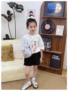 Look mode pour fille avec t-shirt graphique blanc, jupe plissée noire et petit sac argenté