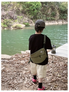 Sac bandoulière enfant en nylon vert armée porté en extérieur près de la rivière