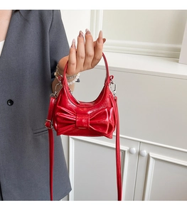 Close-up of bright red patent leather mini handbag with a large bow and silver zipper detail