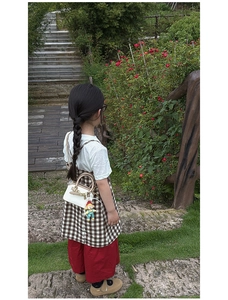 Mini white shell bag for children with brown handle and cute cartoon pendant shown in a park