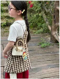 Close-up of children's cream shell handbag with cute cartoon charm and adjustable strap