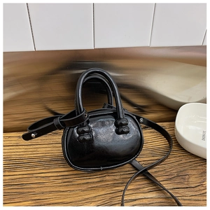 Détail d'un mini sac bowling noir en cuir verni brillant sur surface en bois