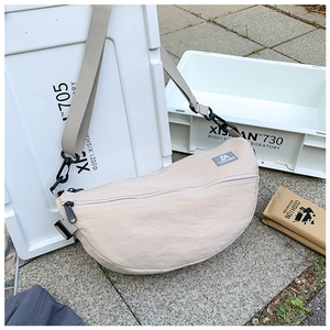 Gros plan du sac bandoulière beige en nylon avec sangle réglable et étiquette de marque