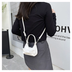 Detail of white mini crossbody bag with 3D bow design worn over a black shoulder
