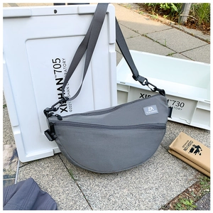 Détail d'un sac bandoulière gris avec sangle réglable sur une boîte de chargement blanche