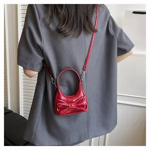 Detail view of mini red glossy handbag featuring a decorative large bow and thin strap