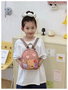 Pink toddler backpack featuring cartoon capybara print shown on a child model in home