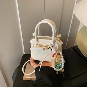 Detail of a white mini shell bag with synthetic leather texture and a pearl cartoon pendant