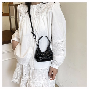Detail view of mini black crossbody bag with large bow and glossy patent leather finish