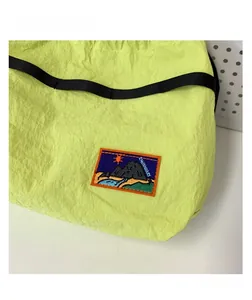 Detail of lime green crinkled fabric and embroidered mountain patch on kids shoulder bag