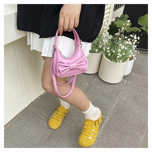 Pink mini crossbody bag with a large bow detail shown in an outdoor street setting