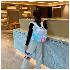 Detail view of a little girl wearing a sky blue cartoon mermaid backpack with floral pattern
