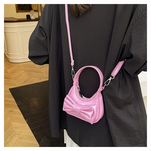 Pink bow mini crossbody bag shown on a person for scale with a stylish glossy finish