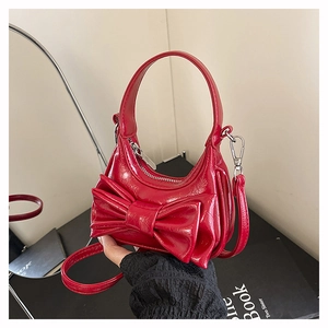 Close-up of a red patent leather half-moon handbag featuring a large stylish bow detail
