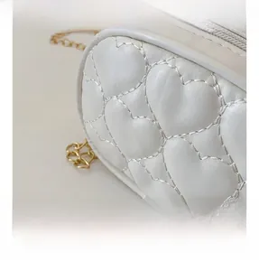 Dettaglio borsa in pelle PU bianca con trapuntatura a cuore e catena dorata