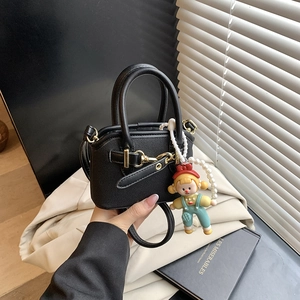 Detail of mini black shell bag with golden buckle and cute doll charm accessory