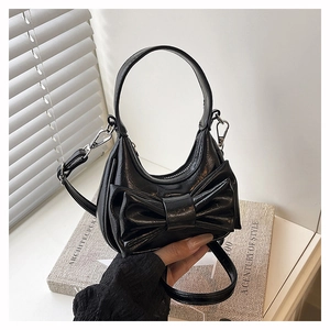 Detail of black glossy handbag featuring a prominent bow design and polished silver hardware