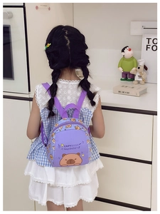 Rear view of a child wearing a purple cartoon Capybara backpack in a cozy room