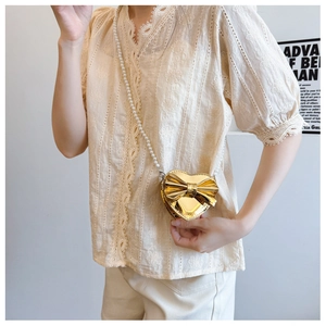Close-up of golden heart-shaped mini bag with bow and pearl strap on model