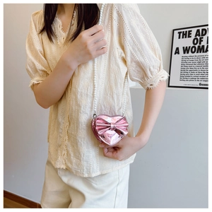 Close-up of heart-shaped mini crossbody bag with a metallic bow and pearl chain