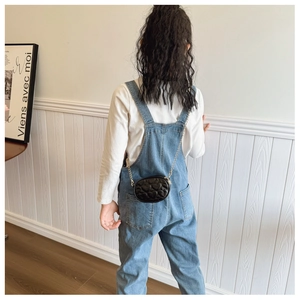 Vista posteriore di una bambina con salopette in denim e borsa a catena a forma di cuore