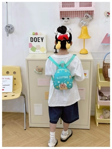 Detail of mint green capybara backpack shown on child model in cozy room setting
