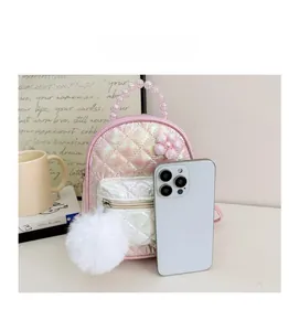 Detail view of mini pink quilted backpack with pearl handle and plush ball charm next to phone