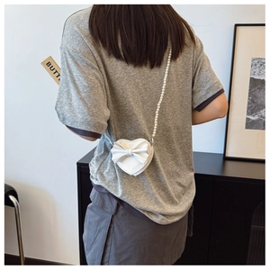 Detail of white heart-shaped girl's crossbody bag with bow and pearl chain strap