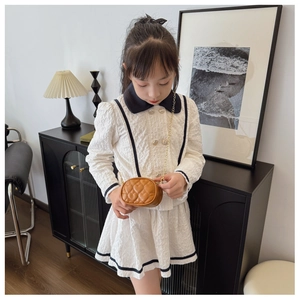 Dettaglio mini borsa trapuntata a cuore con catena d'oro su vestito bianco da bambina