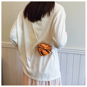 Detail of metallic orange heart bag with large bow and elegant pearl chain strap