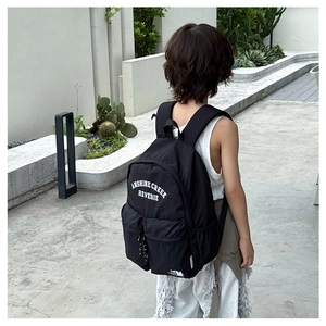 Kid wearing black school backpack with white letter printing in outdoor setting