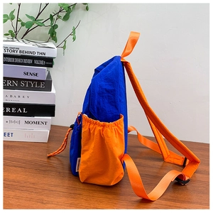 Detail view of the side drawstring pocket on a blue and orange color-block nylon backpack