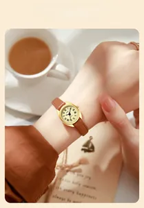 Gros plan d'une montre dorée ovale avec chiffres romains et bracelet en cuir marron au poignet