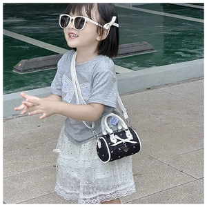 Detail showing white bow and silver heart pendant on kids black cylinder bag