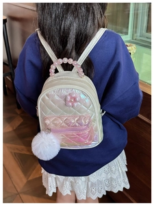 Detail of child backpack with quilted pattern, pearl handle, and plush ball charm