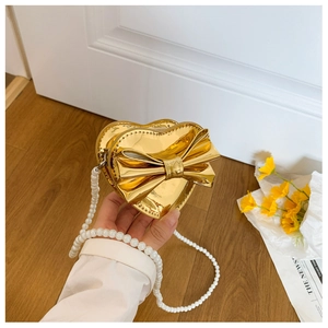 Detail of heart-shaped gold metallic bag with bow decor and elegant pearl chain