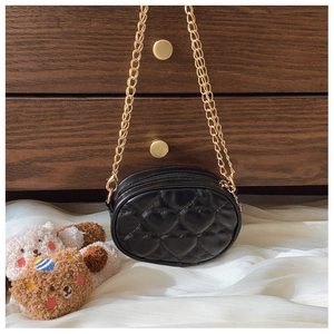 Dettaglio della mini borsa a catena nera trapuntata a cuore su tessuto bianco e legno