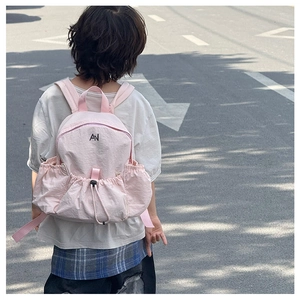 Rear view of child wearing pink drawstring backpack with black AN logo in outdoor street