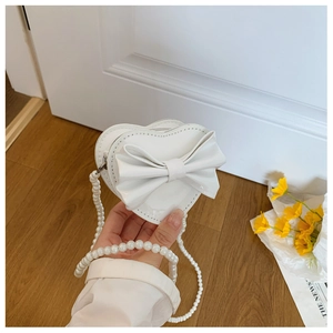 Detail of white heart-shaped mini bag with a large bow and pearl shoulder strap