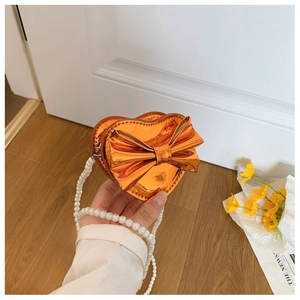Close-up of girls heart-shaped crossbody bag with orange laser finish and pearl strap