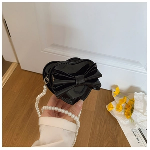 Detail of a mini heart-shaped crossbody bag with glossy bow and white pearl handle